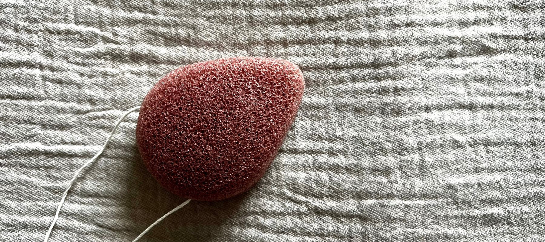 Tear shaped French pink clay konjac sponge for sensitive skin lying on a textured background.